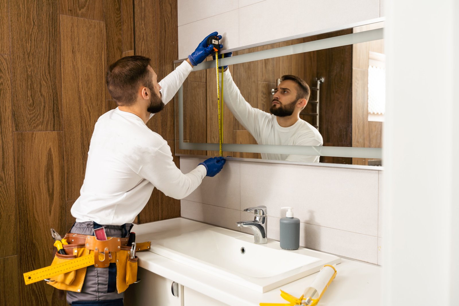 The worker installs the mirror in the bathroom.