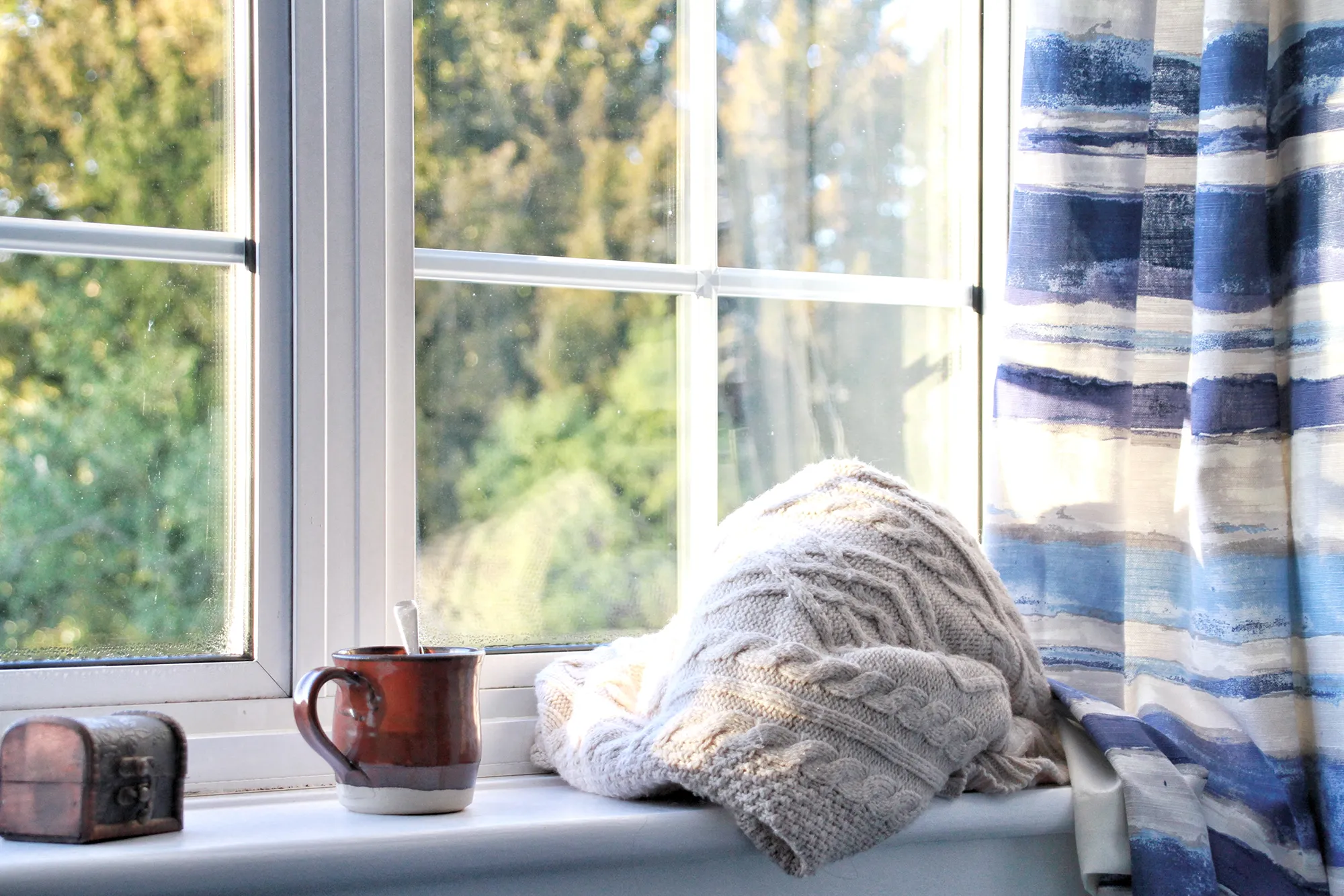 Ljust och tyst rum med ljudisolerande fönster, ett fönsterbleck med mugg, filt och gardiner i förgrunden.