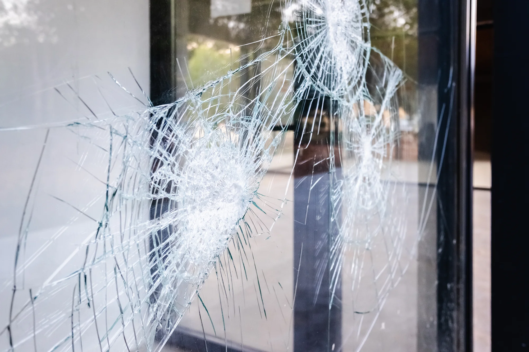 Närbild på krossat säkerhetsglas med spindelnätsmönster, där glaset hålls samman trots kraftiga slag.